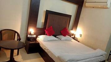 A hotel room with a bed, bedside tables, a chair, and an air conditioning unit.