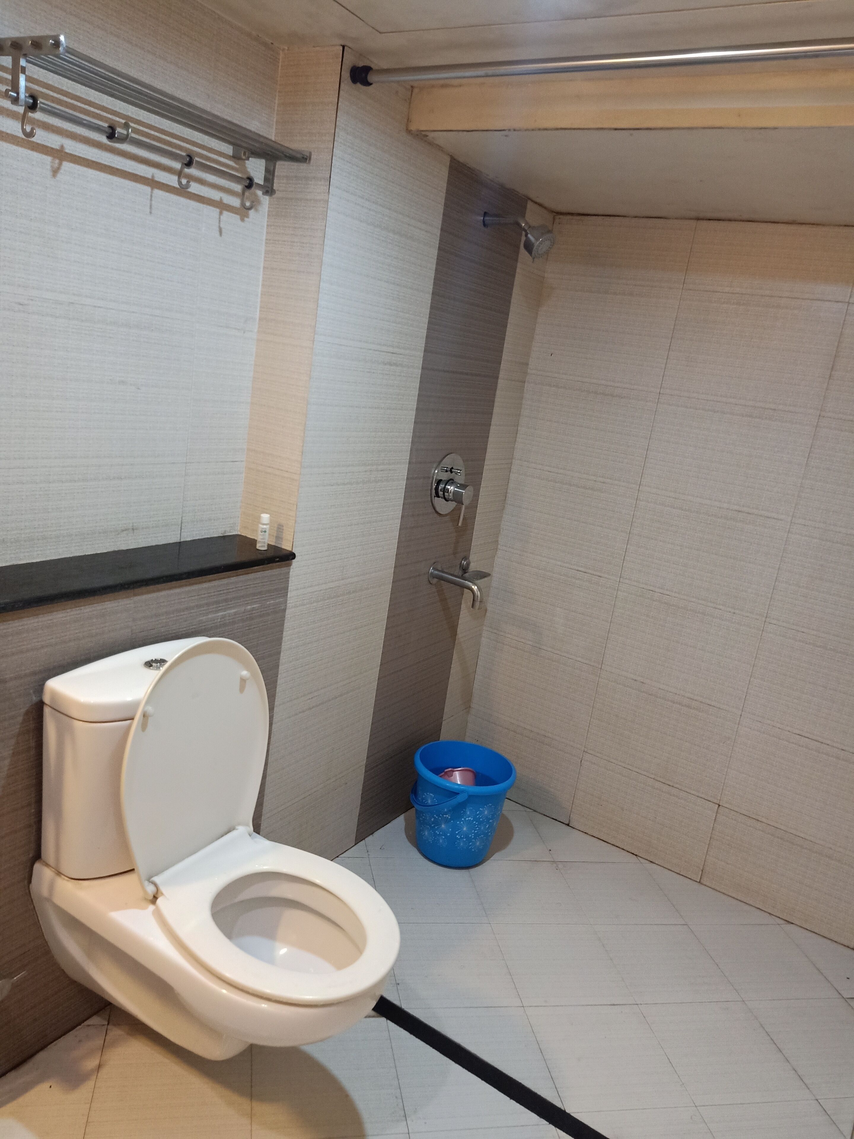 A bathroom with a toilet, a shower, and a blue bucket.