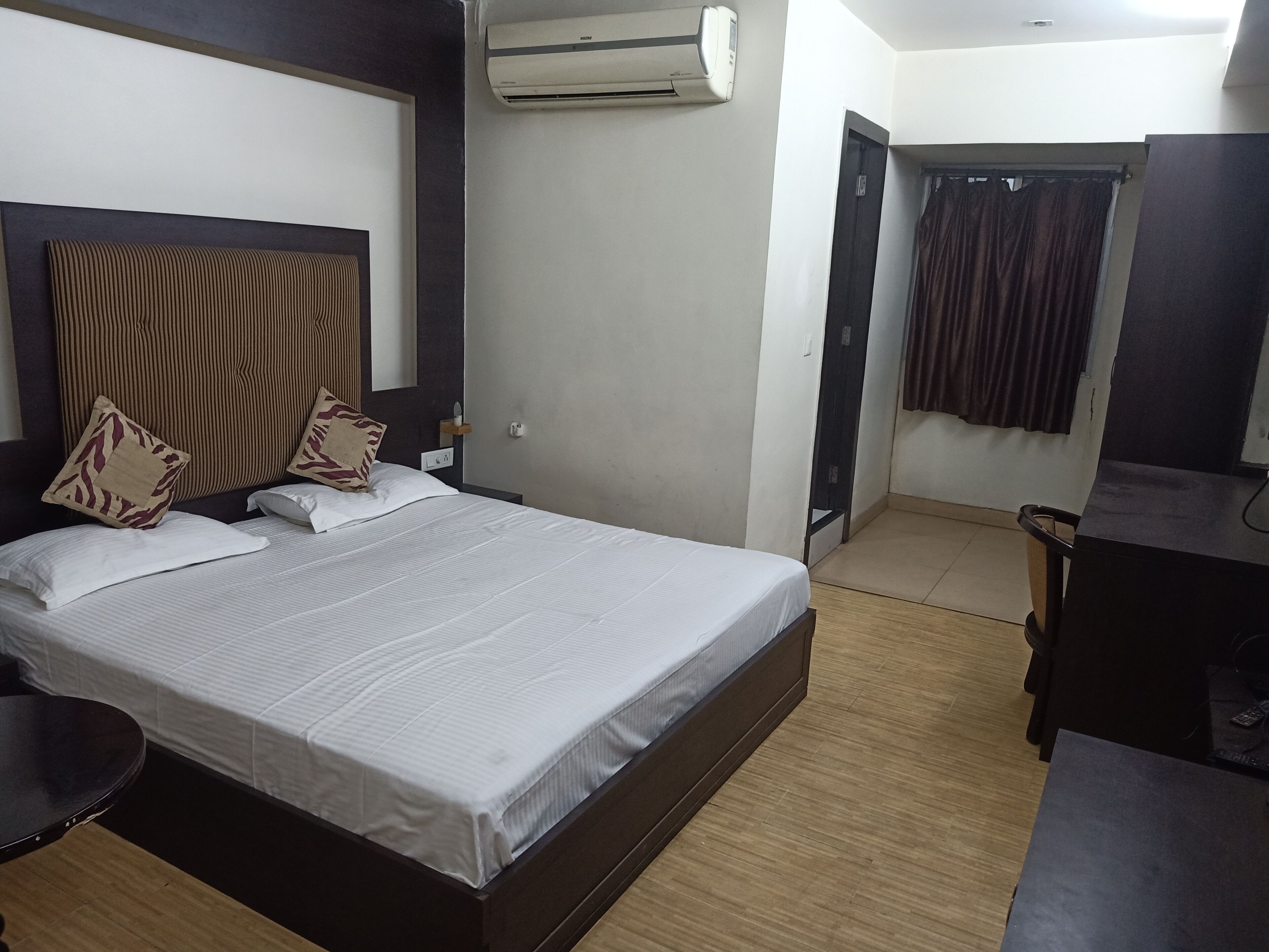 Una habitación de hotel con una cama, un escritorio, un equipo de aire acondicionado, una puerta y una cortina.