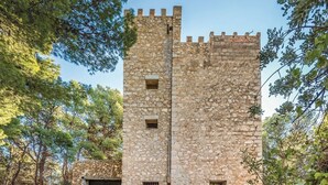 Una torre de piedra con una puerta central y dos ventanas, rodeada de árboles.