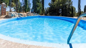 Una piscina azul cristalina rodeada de árboles altos y un muro de piedra.