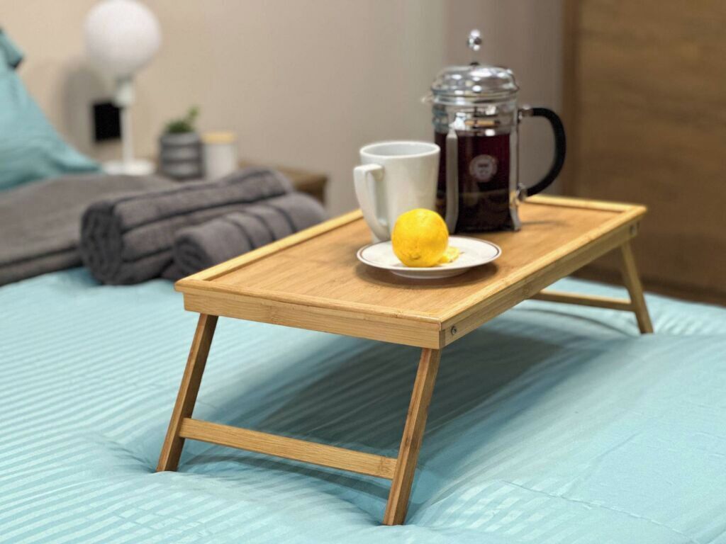 Een houten dienblad met een koffiepot, een mok en een citroen op een bed.
