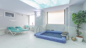 Un cuarto de spa con un jacuzzi de azulejos azules, dos sillones de descanso verdes, un techo con diseño de nubes y una planta en maceta.
