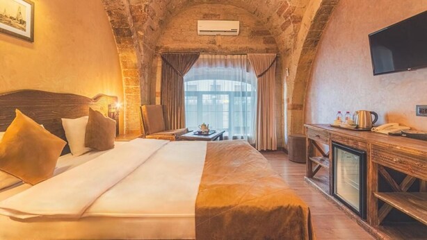 Habitación de hotel con una cama grande, un escritorio con teléfono y cafetera, un televisor montado en la pared y una ventana con cortinas.