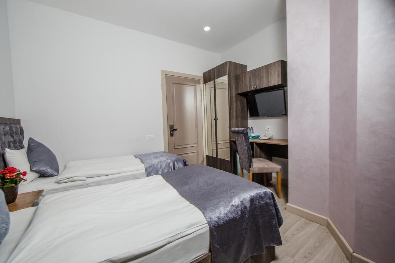 A hotel room with two beds, a desk, a TV, and a door.