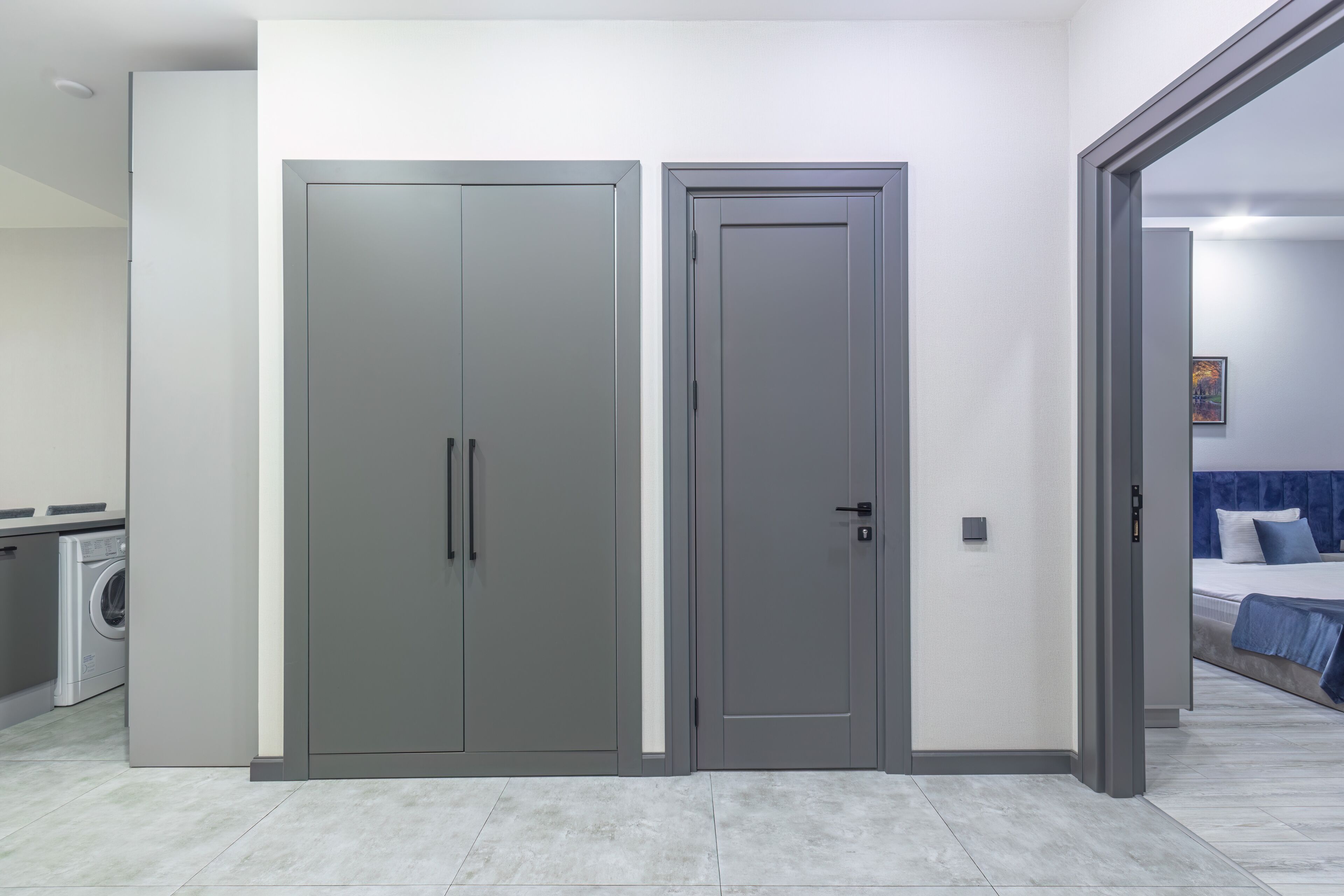 A modern room with two grey doors, a washing machine, and a bed with blue bedding.