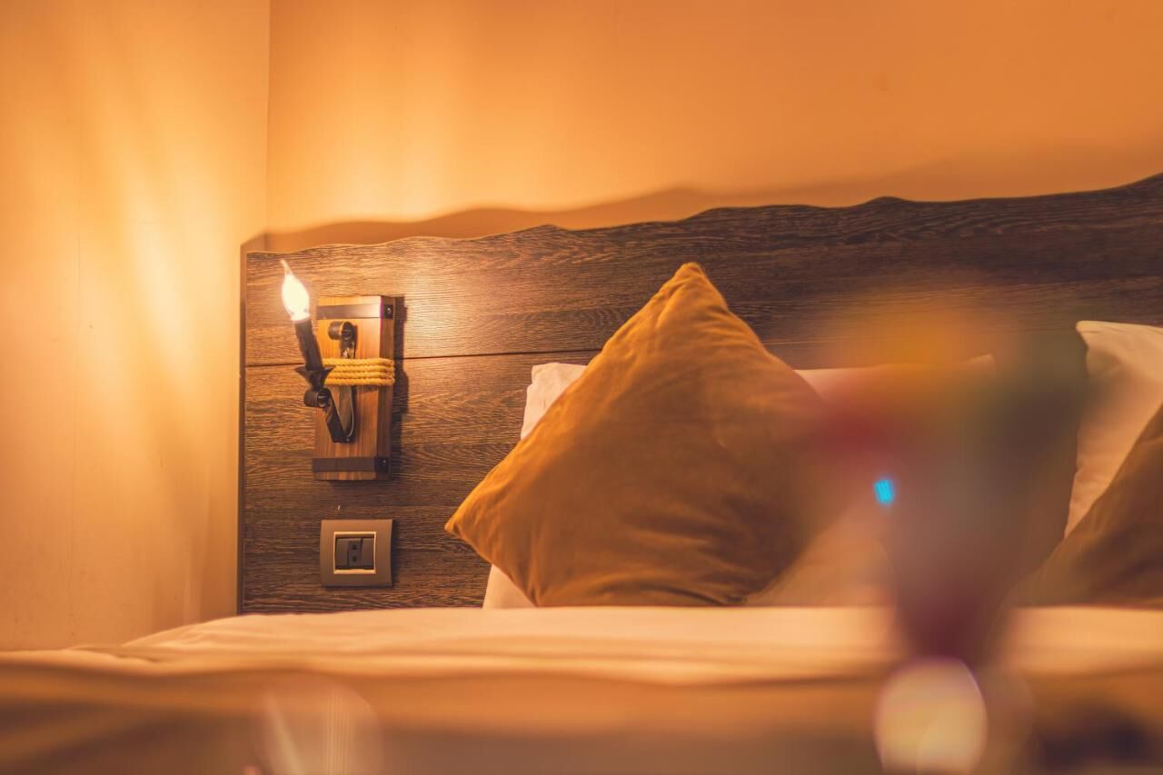 A neatly made bed with a wooden headboard, a wall-mounted light fixture, and a power outlet.