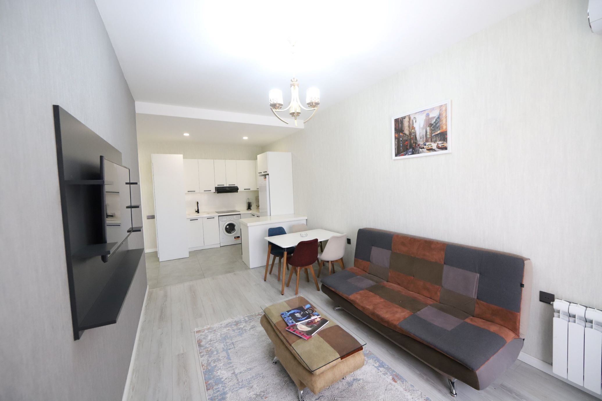 Una sala moderna con un sofá, una mesa de centro, un televisor y una cocina al fondo.