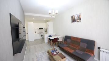 Una sala moderna con un sofá, una mesa de centro, un televisor y una cocina al fondo.