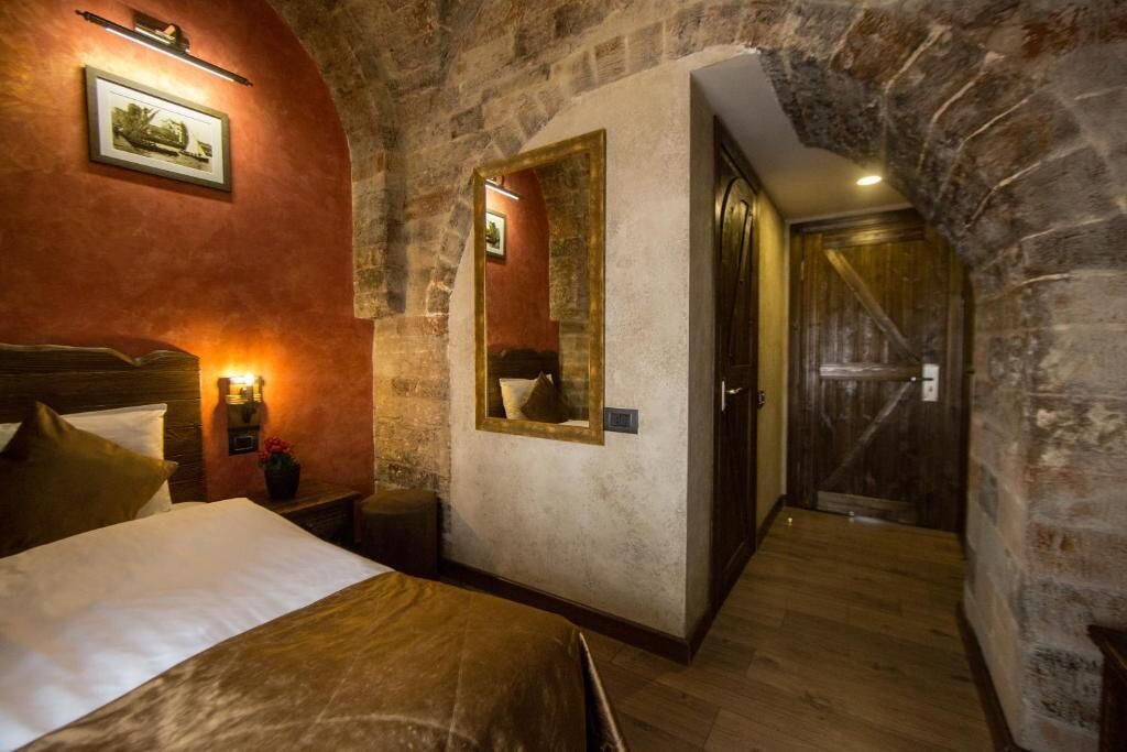 A hotel room with a large bed, a nightstand, a mirror, and a wooden door.