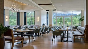 Un restaurant doté de grandes fenêtres, de tables et de chaises en bois, et offrant une vue sur la verdure et les montagnes.
