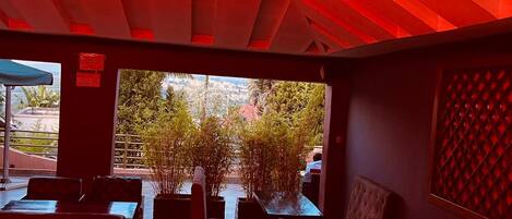 An interior with red lighting, seating, and a view of greenery outside.