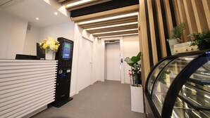 A reception area with a modern design, including a reception desk, self-service kiosk, and an escalator. - Hwagokhoteln (Seoul)