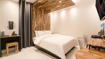 A modern hotel room with a large bed, a desk with a chair, a round table with chairs, a TV, and a wooden ceiling design.