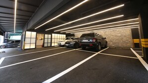 An underground parking garage with multiple cars parked, illuminated by linear lights on the ceiling. - Hwagokhoteln (Seoul)