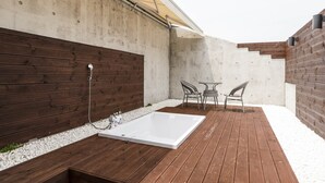 A patio with a wooden deck, a white bathtub, two wicker chairs, and a concrete wall with a wooden panel. - Hwagokhoteln (Seoul)