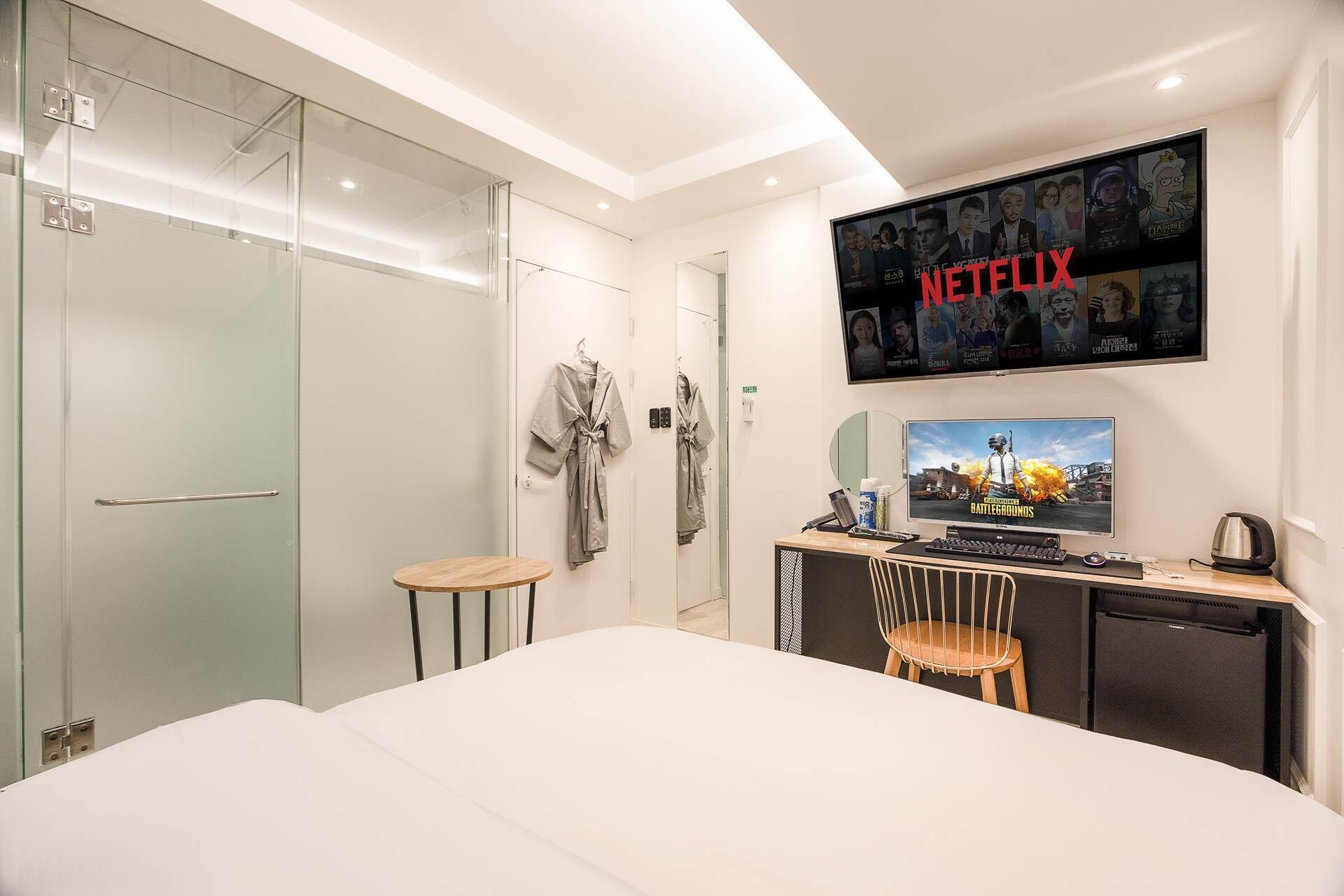 Ein Hotelzimmer mit Bett, Schreibtisch mit Computer, Fernseher mit Netflix und einer Duschkabine aus Glas.