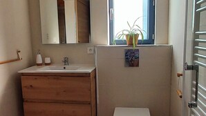 Ein Badezimmer mit einem Holzbadezimmerschrank, einer Toilette, einem Fenster mit Pflanze und einem Spiegel.