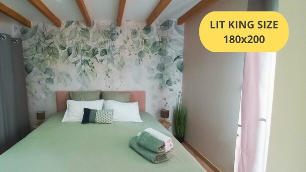 Ein Schlafzimmer mit Bett, Kissen und Nachttisch. Die Wände sind mit floralem Wandpapier versehen und die Decke ziert sich mit Holzbalken.