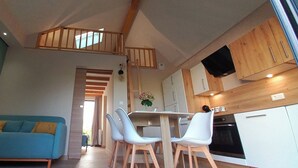 Ein moderner Wohnraum mit einem blauen Sofa, weißen Sesseln, einem Esstisch und einer Küchenzeile mit Holzschränken sowie einem Fernseher.