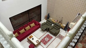 Un salón con chimenea, sofás rojos y verdes, una mesa de centro y alfombras estampadas.