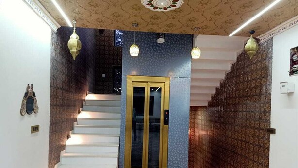 Una escalera con una puerta de cristal, un muro decorado y una araña.