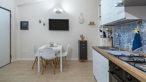 Eine moderne Küche mit eingebautem Herd, einem Essbereich mit weißem Tisch und Stühlen sowie einem an der Wand befestigten Flachbildfernseher.