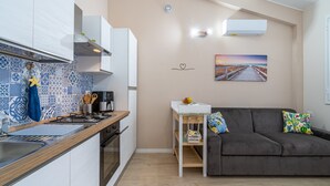 Ein kompakter Wohnbereich mit Küchenzeile, einer Couch, einem kleinen Tisch und einem Bild an der Wand.