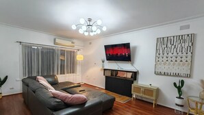 Een moderne woonkamer met een zwarte leren bank, een flatscreen-tv aan de muur, een vloerlamp en een decoratief wandobject.