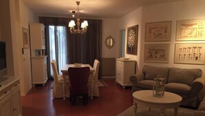 A living room with a dining table, sofa, and a coffee table. There is a chandelier, a radiator, and framed pictures on the wall. - Residence of the TOLOMEI - SACILE (Sacile)