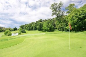 A golf course with a flagstick, trees, and a pond. - Residence of the TOLOMEI - SACILE (Sacile)
