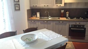 A compact kitchen with white cabinets, a sink, a stove, and a dining table with chairs. - Residence of the TOLOMEI - SACILE (Sacile)