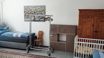 Ein modernes Wohnzimmer mit grauem Sofa, einem weißen Babybett, einem Holzschrank und einem Metallwagen.