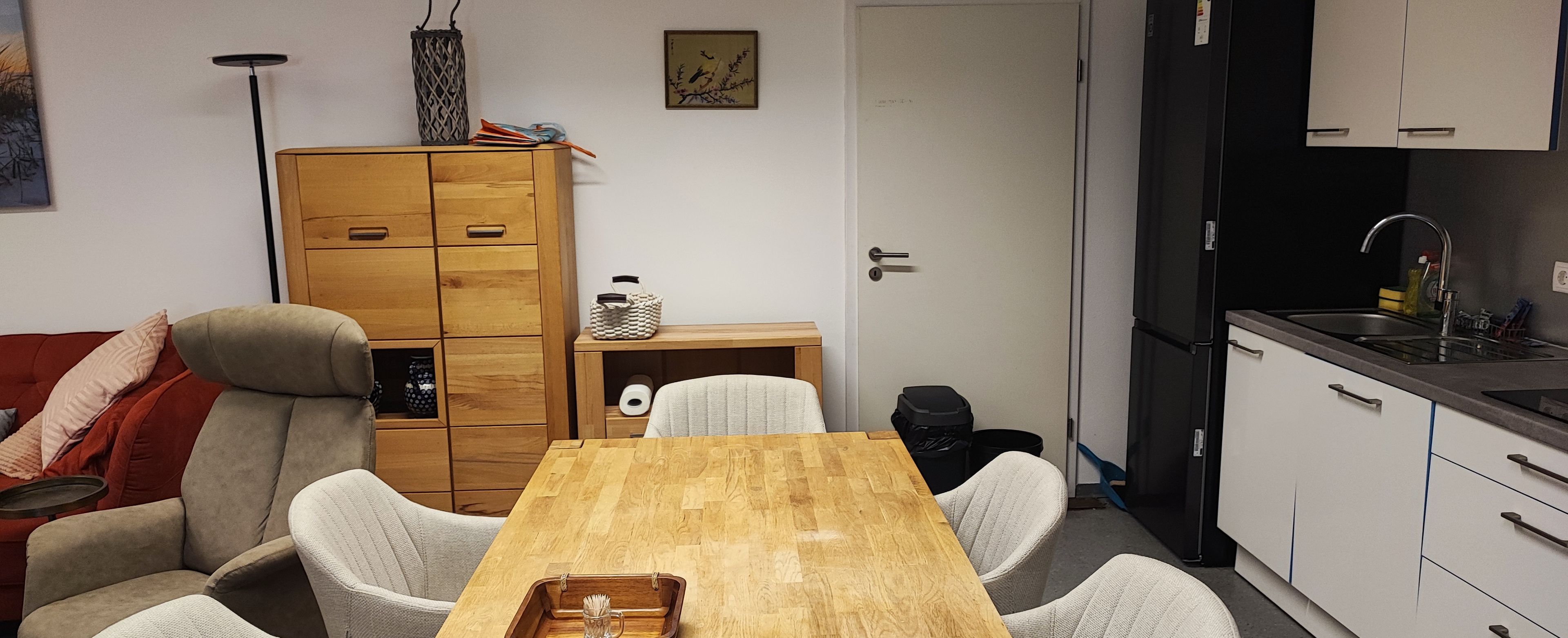 Ein kompakter Wohnraum mit Esstisch aus Holz, einer Couch, einem kleinen Schrank und einer Küchenzeile.