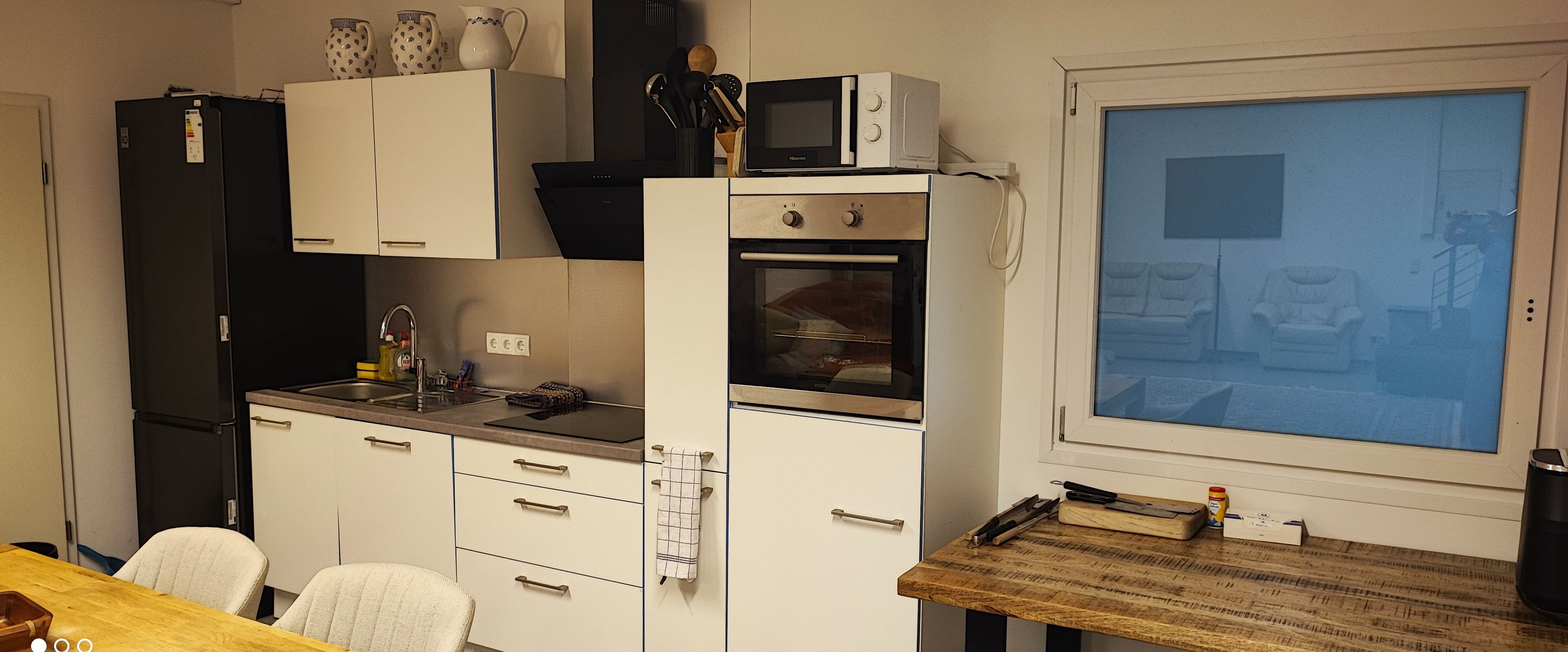 Une cuisine compacte équipée d’un four à micro-ondes, d’un four et d’un évier. On y trouve une table à manger avec des chaises et une grande fenêtre.