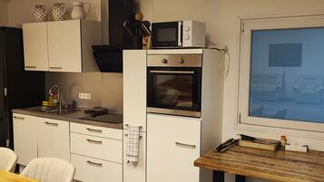 Une cuisine compacte équipée d’un four à micro-ondes, d’un four et d’un évier. On y trouve une table à manger avec des chaises et une grande fenêtre.