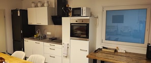 Une cuisine compacte équipée d’un four à micro-ondes, d’un four et d’un évier. On y trouve une table à manger avec des chaises et une grande fenêtre.