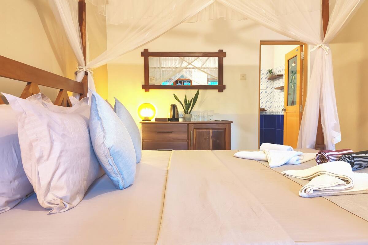 A bedroom with a canopy bed, a bedside table with a lamp, and a mirror on the wall.