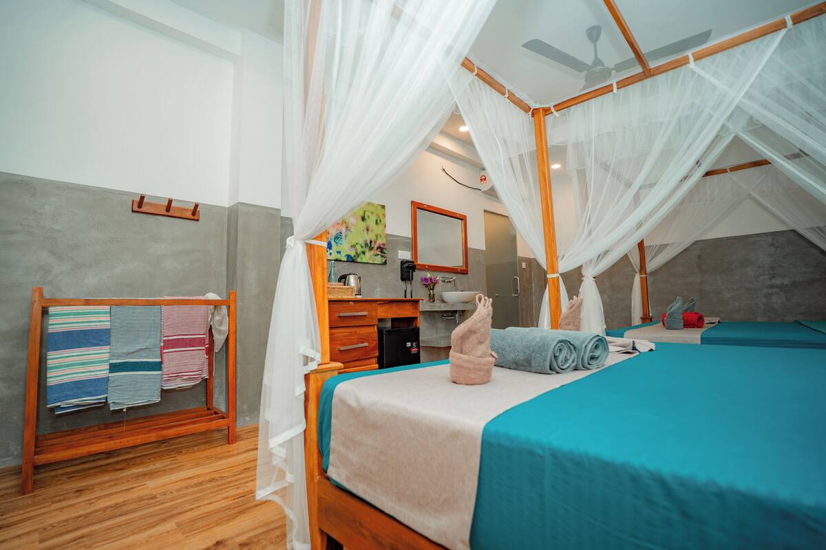 A bedroom with a canopy bed, a wooden bedside table, a mirror, and a wall-mounted shelf with towels.