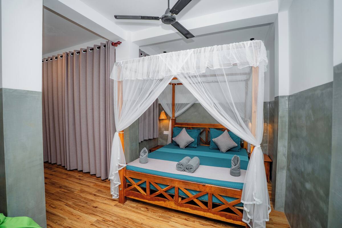 A four-poster bed with a canopy, wooden frame, teal bedding, and grey pillows.