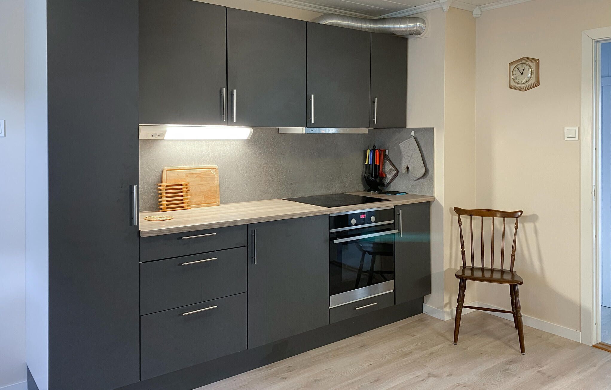 A modern kitchen with dark cabinets, a wooden countertop, a built-in oven, and a chair.