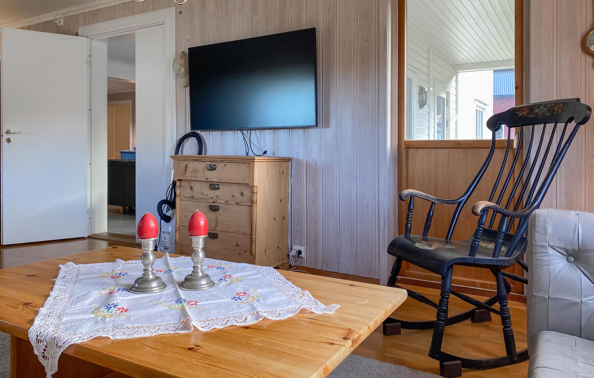 Una mesa de comedor de madera con mantel de encaje, dos saleros y pimenteros, y un mueble de madera con un televisor encima.