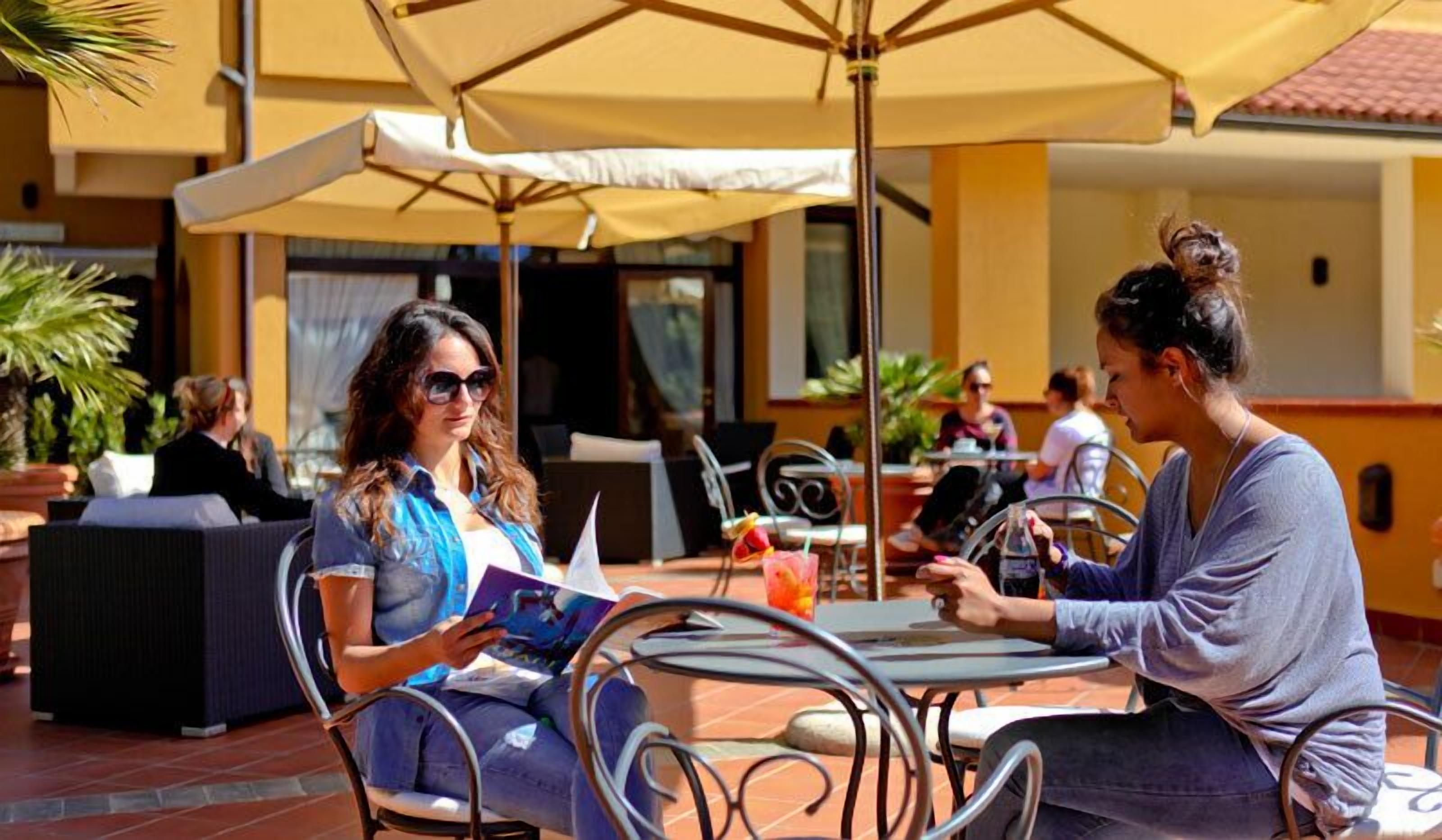 An outdoor café with tables and chairs, umbrellas, and potted plants.