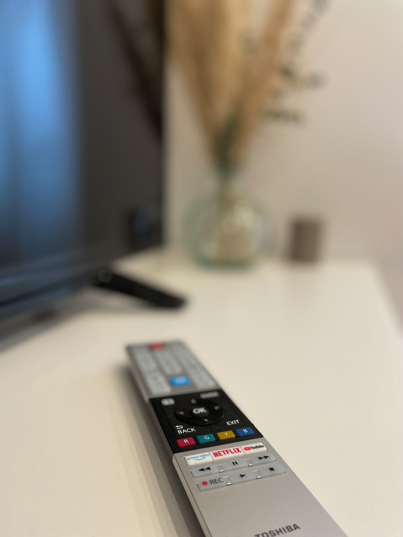 Une télécommande posée sur une table, avec un téléviseur en arrière-plan.