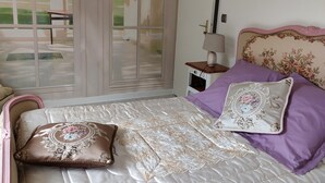 Une chambre à coucher avec un lit, une table de chevet, une lampe et une vue sur un jardin, visible à travers une porte vitrée.