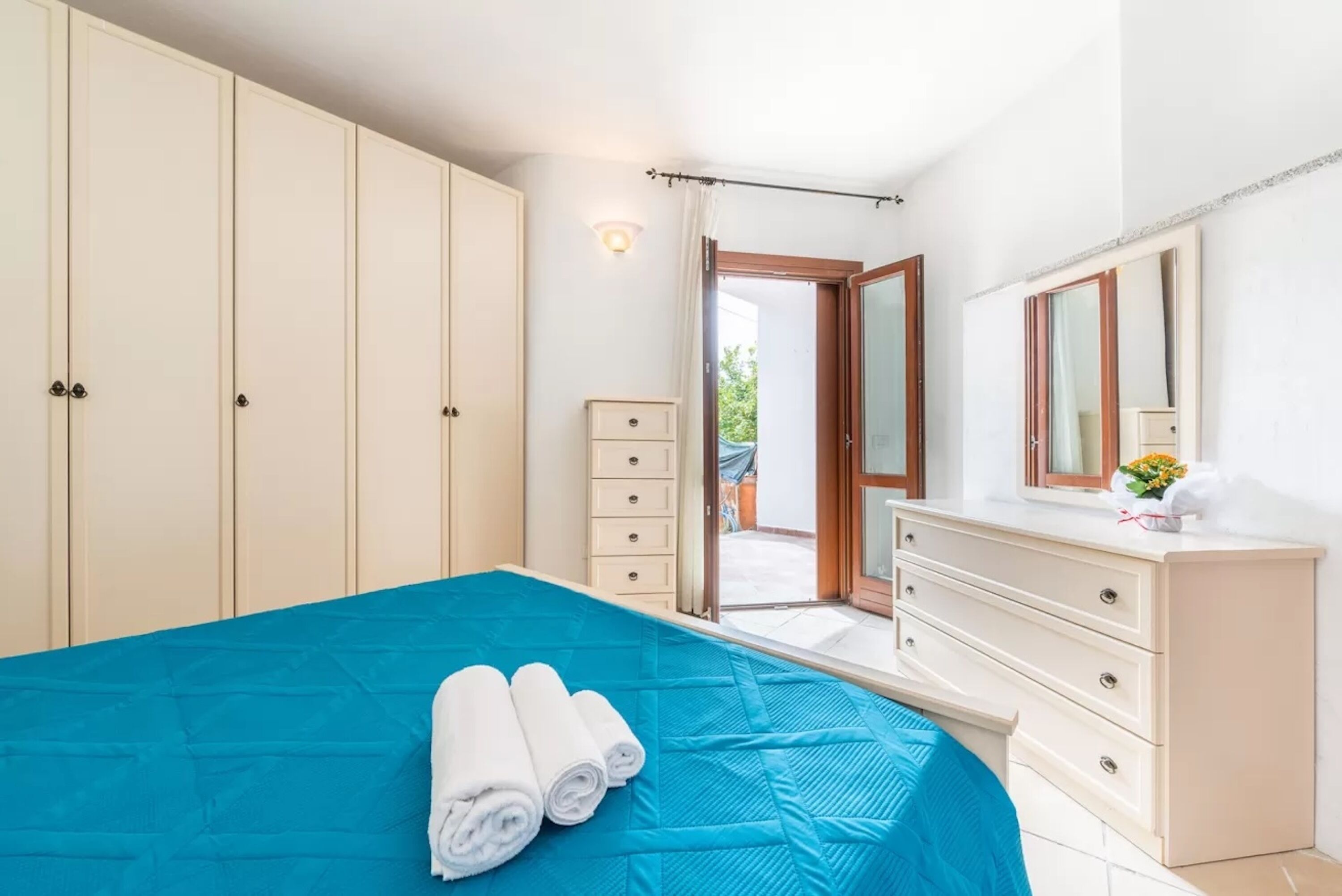 A bedroom with a bed, a dresser, a mirror, and a door leading to an outdoor area.