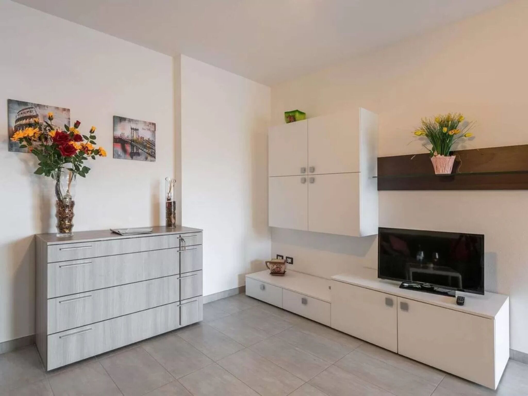 Un salon moderne avec un meuble gris, un téléviseur à écran plat et deux meubles fixés au mur.