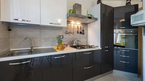 A modern kitchen with black and white cabinetry, stainless steel appliances, and a central island with a sink and fruit bowl. - Seaside comfort in the heart of Alghero (Alghero)