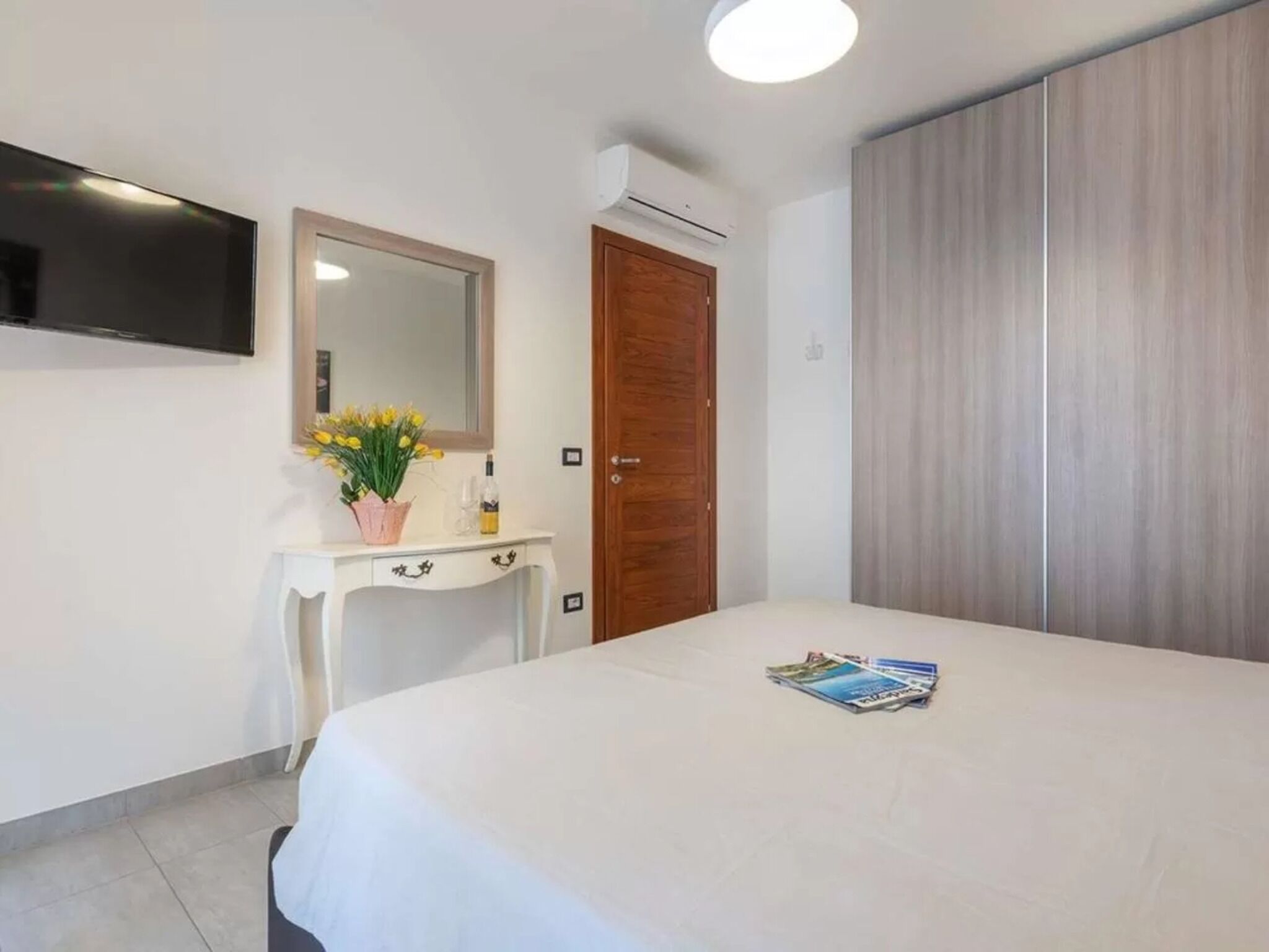 A bedroom with a bed, a dresser, a mirror, a TV, and a wardrobe.