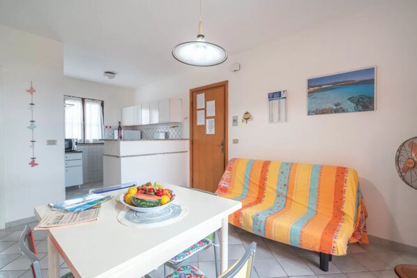 Un espacio habitable compacto con una mesa de comedor, un sofá colorido, una zona de cocina y vistas al mar.